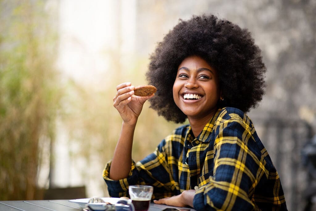Portrait of happy young black woman eating cookie