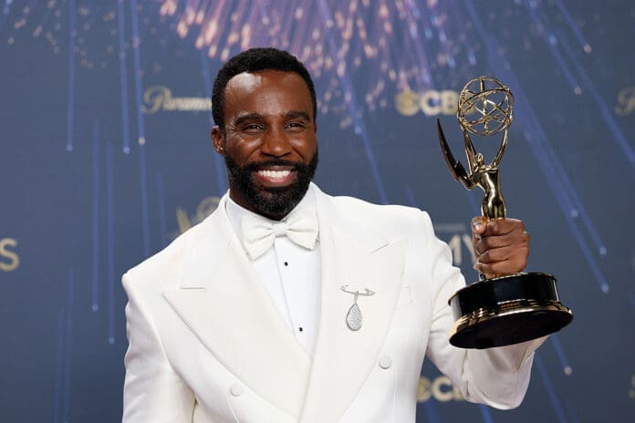 Tramell Tillmsn in s white tux holding his Emmy